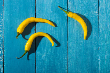 Canvas Print - three yellow chili peppers on blue wooden table background