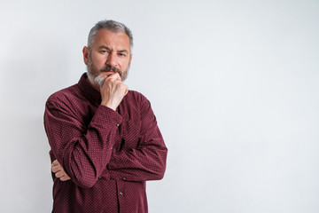 Wall Mural - Half-length portrait of a serious gray-haired bearded man in a burgundy shirt on a white background