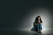 Lonely woman with smart phone sitting on floor in dark room. Space for text