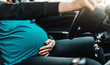 Close up of pregnant woman driving car. One hand on steering wheel and other on belly.