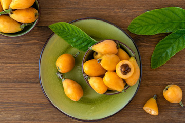 Wall Mural - Loquat fruit. Nispero. Eriobotrya Japonica. Loquat in plate with fresh leaves on wood background	