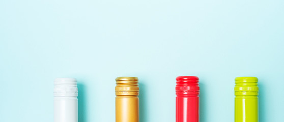 Wall Mural - Screw bottle foil caps in different bright colors of white and rose wine bottles on blue background with copy space. Minimal abstract colorful mockup concept of alcohol beverage. Flat lay.