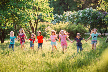 Large group of kids, friends boys and girls running in the park on sunny summer day in casual clothes .