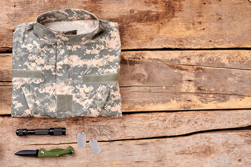 Camouflage shirt and accessories. Top view, flat lay. Wooden desk surface background.