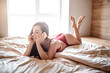 Seductive young naked dark-haired woman in bed on morning. Lying and talking on phone. Wearing red lingerie. Slim sexy well-built woman relaxed and peaceful.