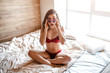 © estradaanton - Seductive young naked dark-haired woman on bed in morning. Amazed sensual model sitting with legs crossed and touch sunglasses with hands. Sexy brunette in room.