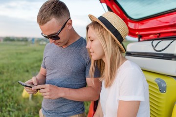 Wall Mural - Young couple sitting in the trunk of a car on a summer day close-up looking at the phone screen going to camping with friends