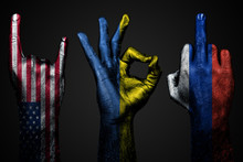A Set Of Three Hands With A Painted Flag Of Ukraine, Russia And USA Show Middle Finger, Goat And Okay, A Sign Of Aggression, Protest And Approval On A Dark Background.