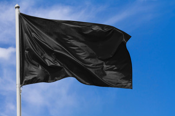 Wall Mural - Black flag waving in the wind on flagpole against the sky with clouds on sunny day, closeup