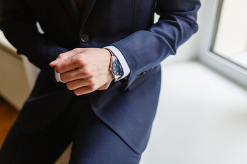 Wall Mural - Close-up of a man in an expensive tailored suit straightens shirt cuffs. Man sitting on the windowsill by the window