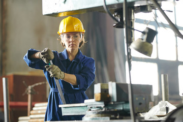 Waist up portrait of mature woman working at factory and using industrial machines, copy space