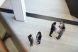 © Seventyfour - Directly above view of intercultural business people in formal outfits standing in groups in lobby and discussing ideas for projects