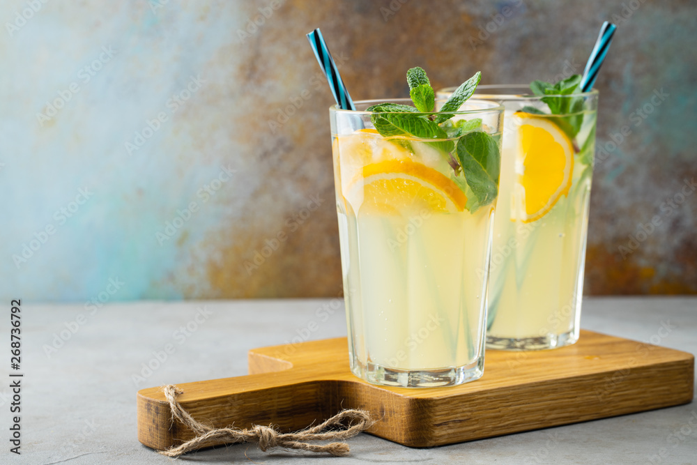 Two glass with lemonade or mojito cocktail with lemon and mint, cold refreshing drink or beverage with ice on rustic blue background. Copy space - obrazy, fototapety, plakaty 