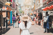 Young Woman Traveling With White Dress And Hat, Happy Asian Traveler Walking At Chinatown Street Market In Singapore. Landmark And Popular For Tourist Attractions. Southeast Asia Travel Concept