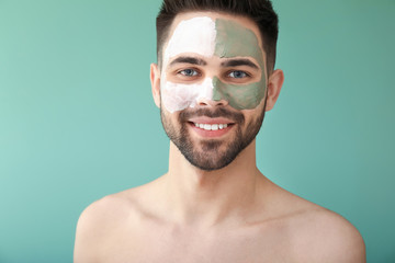 Handsome man with clay mask on his face against color background