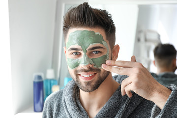 Wall Mural - Handsome man applying clay mask onto his face at home