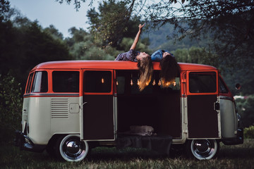 Two girl friends at dusk outdoors on a roadtrip through countryside, having fun.