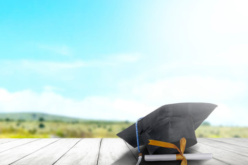 Mortarboard hat and diploma on wooden table with landscapes and blue sky background