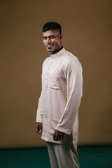 Studio portrait of a young, handsome and athletic Malaysian Indian Muslim Asian man in a cream colored traditional baju melayu tunic. He is dressed festively to go visiting for Raya. 