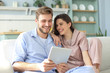 © ty - Young couple watching media content online in a tablet sitting on a sofa in the living room.