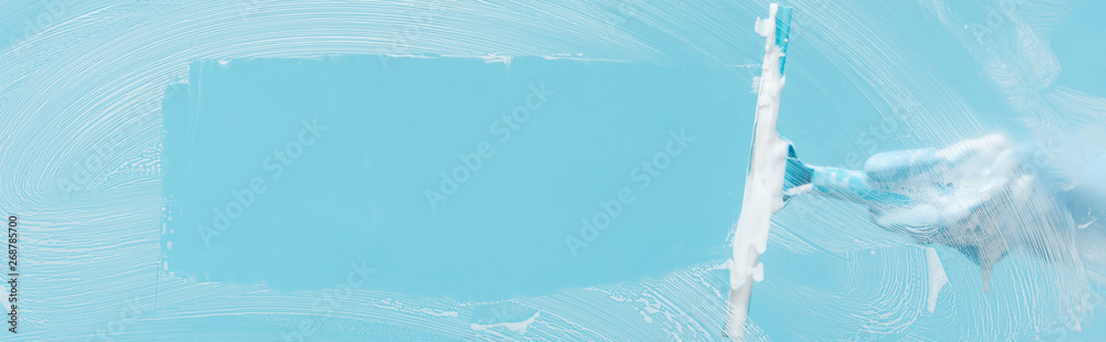 panoramic shot of woman in rubber glove cleaning glass with squeegee on blue background - obrazy, fototapety, plakaty 