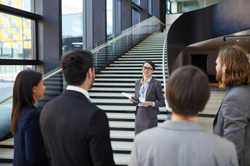 smiling confident business forum guide with badge on neck standing on stairs and holding clipboards 