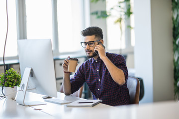 Indian businessman is working on his computer in the office and talking by phone.