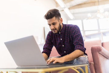 Casual young indian man using laptop with happy on sofa in modern office