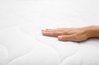 Woman's hand touching cloth white mattress. Checking softness. Choice of the best type and quality. Side view. Closeup.