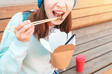 Wall Mural - Fashionable asian teen hipster girl eats Oriental wok noodles with chopsticks. Concept of lunch and natural takeaway containers made of paper