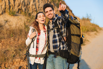 Wall Mural - Cheerful young couple carrying backpacks hiking together