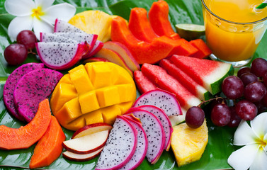 Tropical fruits assortment with fresh juice, palm leaf background. Top view. Close up.