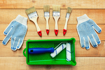 Composition from painting tools with paint brushes, gloves and paint roller on the wooden background