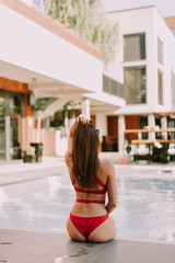 Wall Mural - Attractive young woman in red bikini sits by the poolside and enjoys the summer sun