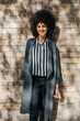 © guille Faingold/Stocksy - Beautiful smiling woman with afro hair in casual look over brick wall.