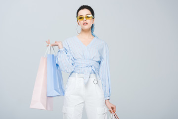 beautiful fashionable girl with shopping bags looking at camera isolated on grey