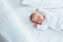 A Sleeping Baby In A White Sleepsuit Lysing On A White Background
