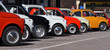  A row of colorful vintage Fiat 500 s  in a roadside parking lot on a sunny day.