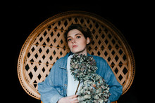 Portrait Of A Beautiful Androgynous Teen Woman Sitting In A Wicker Chair Holding Some Dry Hydrangeas