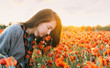 Romantic girl smelling a poppy flower in field.