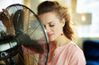 © Alliance - relaxed housewife enjoying fresh air in front of working fan