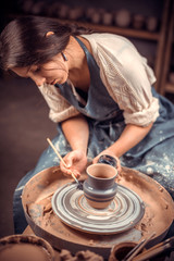 Wall Mural - Charming young and cheerful woman demonstrates the process of making ceramic dishes using the old technology. Handmade products.