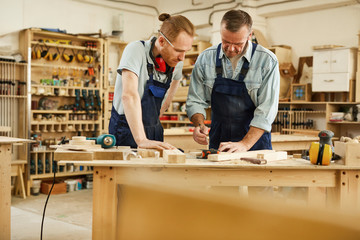 Portrait of senior carpenter teaching apprentice  standing at table in workshop, copy space