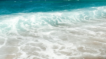 Beautiful image of turquoise sea waves rolling over the shore at bright sunny day