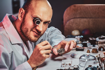 Wall Mural - Mature clockmaster is fixing old watch for a customer at his busy repairing workshop.