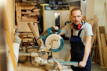 Wall Mural - Waist up portrait of carpenter looking at camera while standing by disksaw in joinery, copy space