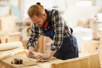 Wall Mural - Portrait of modern carpenter marking wood while working in joinery lit by sunlight, copy space