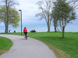 © Spiroview Inc. - A cyclist rides on the trail while others sit in the park enjoying the view of Lake Ontario from Toronto's waterfront trail.