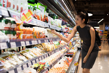 Mother Asian Working woman select pick up healthy nutrition food, yogurt milk from supermarket shelf rack after work. Concept decision Making choice select best thing for kid children family