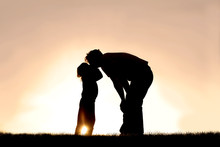 Silhouette Of Little Child Kissing Her Father At Sunset On A Summer Day